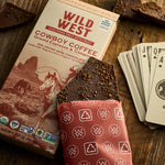 Lifestyle image of a Wild West Cowboy Coffee chocolate bar and box with on a wooden surface with playing cards.