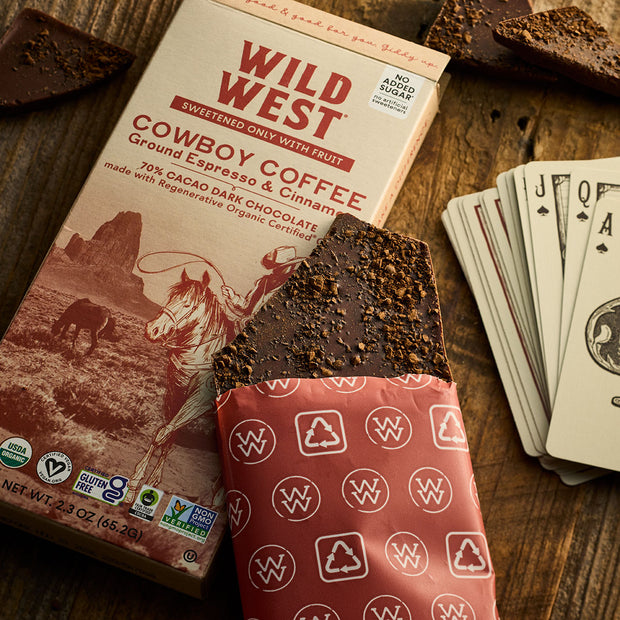 Lifestyle image of a Wild West Cowboy Coffee chocolate bar and box with on a wooden surface with playing cards.