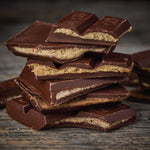 A stack of broken nut butter filled chocolate bars with the real nut butter filling, photographed close-up on a rustic dark wooden surface.