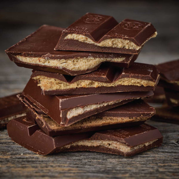 A stack of broken nut butter filled chocolate bars with the real nut butter filling, photographed close-up on a rustic dark wooden surface.