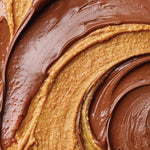 Close-up of a thick, creamy nut butter swirl with glossy chocolate spread layered on top, showing rich brown and warm tan textures.
