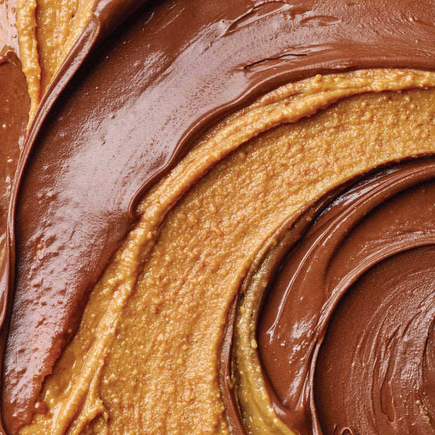 Close-up of a thick, creamy nut butter swirl with glossy chocolate spread layered on top, showing rich brown and warm tan textures.